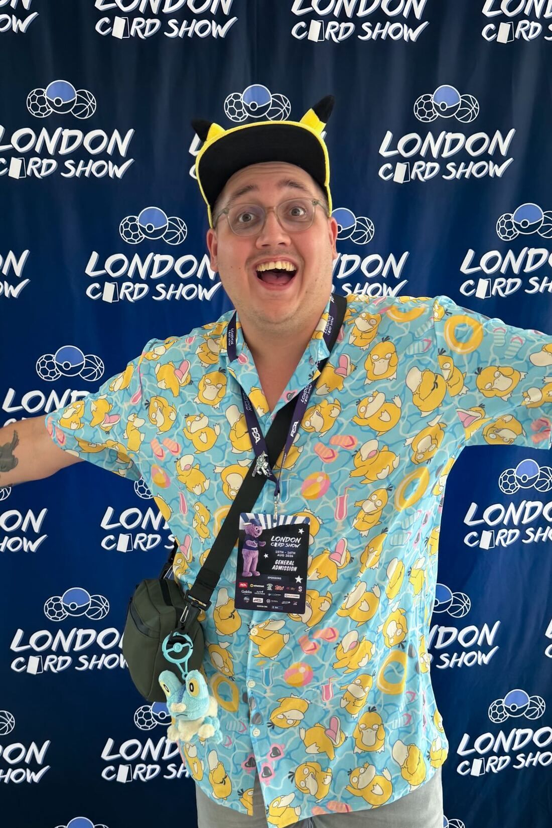 Duncan met Pikachu-pet en Psyduck-overhemd voor de fotowand van de London Card Show